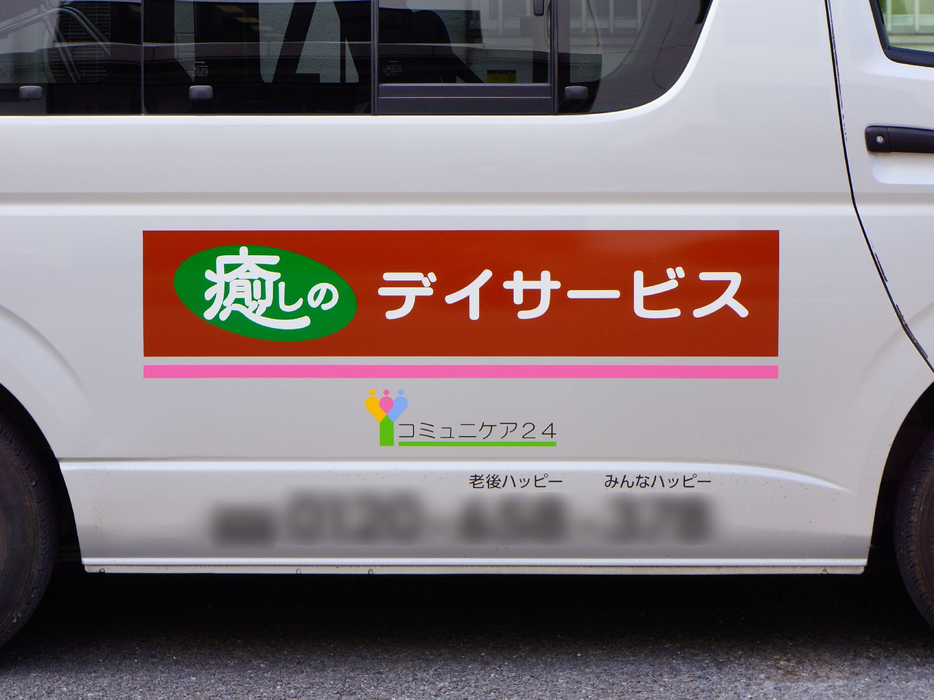 茶色に緑と白とピンクでデザインされたキャッチコピーが灰色の車の側面に入っている。下には施設名も小さく入っている。