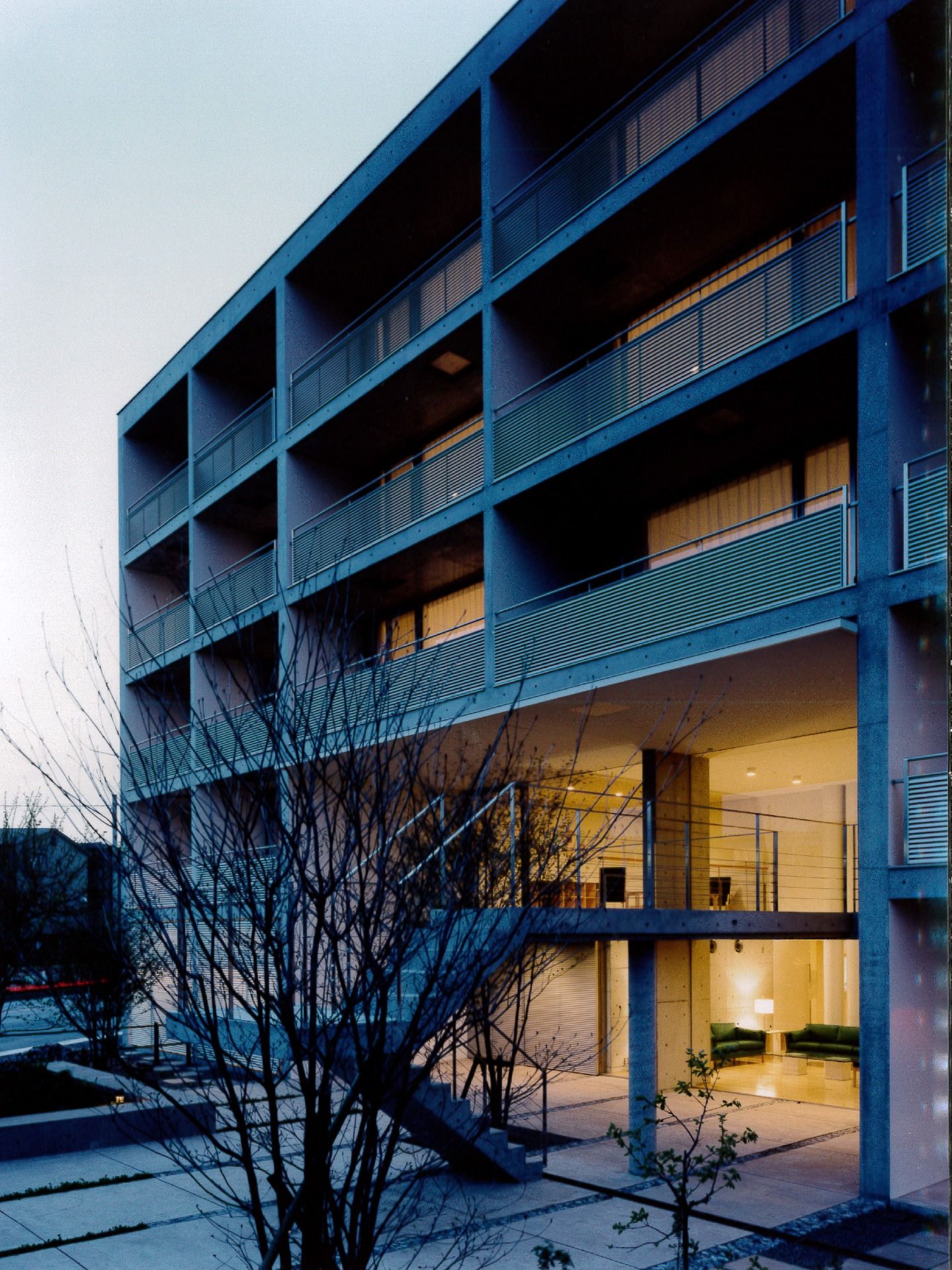 夕闇の中で照明が浮かび上がる建物の写真。中庭が手前にある様子が分かる