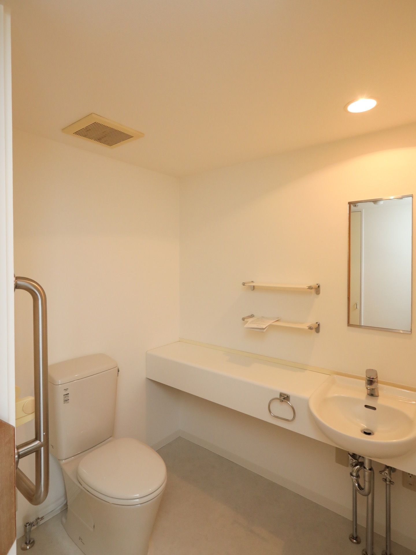 居室のトイレである。広いスペースが確保されており、洗面台が完備されている。壁には、棚や鏡がある。