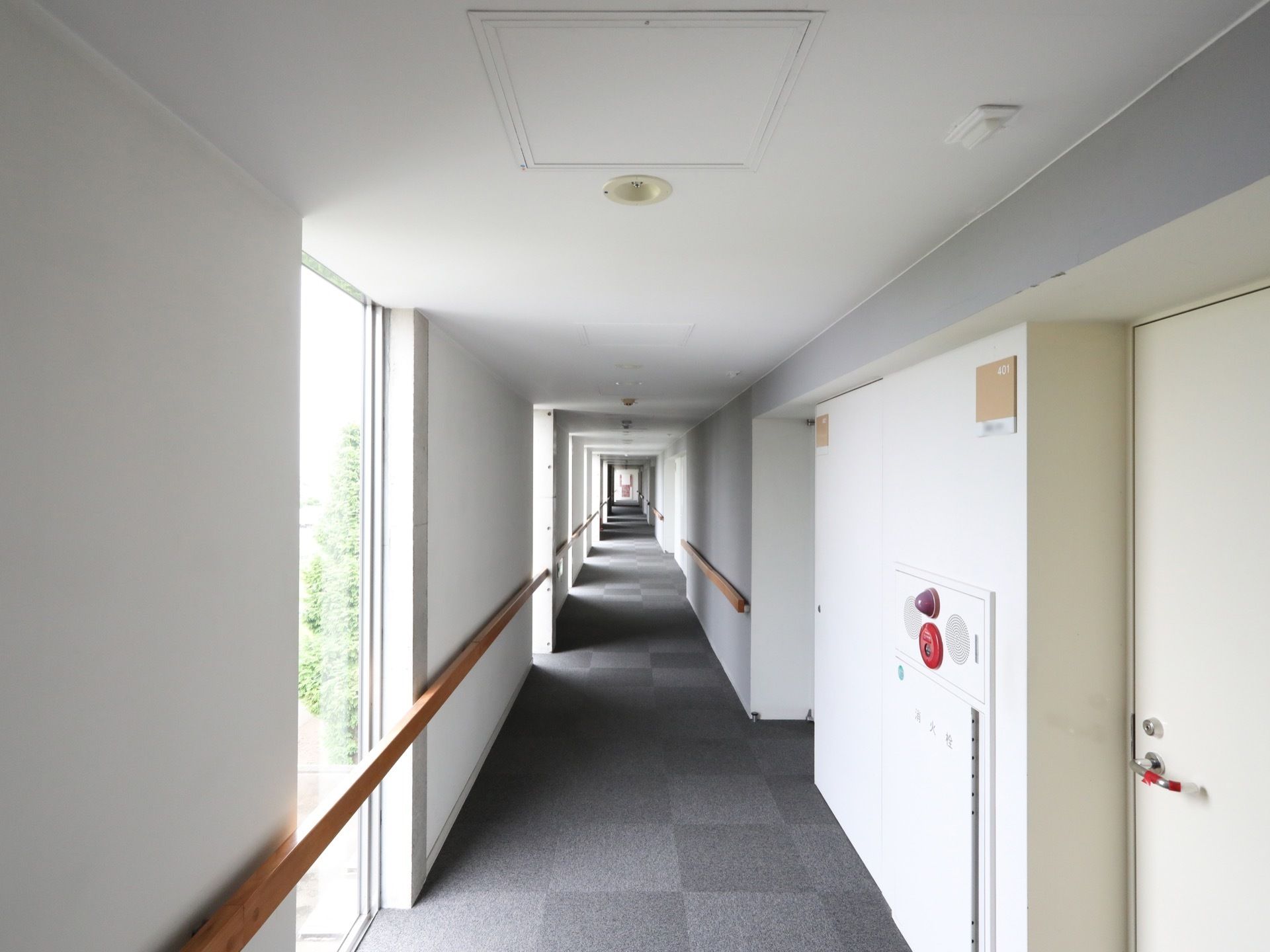 真っ直ぐな廊下である。手すりが両サイドの壁に沿って設置されている。右側には、等間隔で縦長の窓が設けられている。