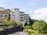 マンションのような建物が２棟並んで立っている。周辺にはたくさんの緑が茂り、青空には入道雲のような雲がわいている。