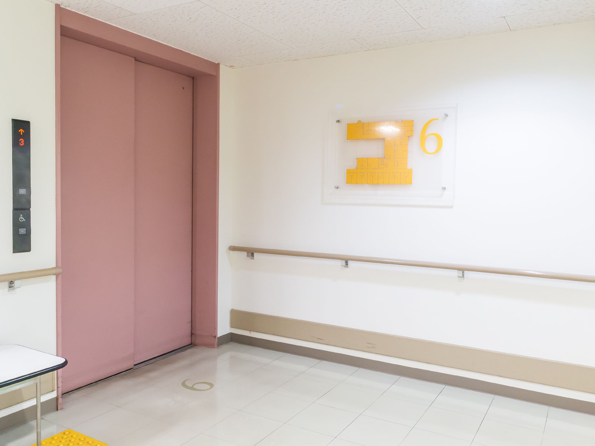 手すりのついた白い壁に配置されているピンクの扉が閉まったエレベーター