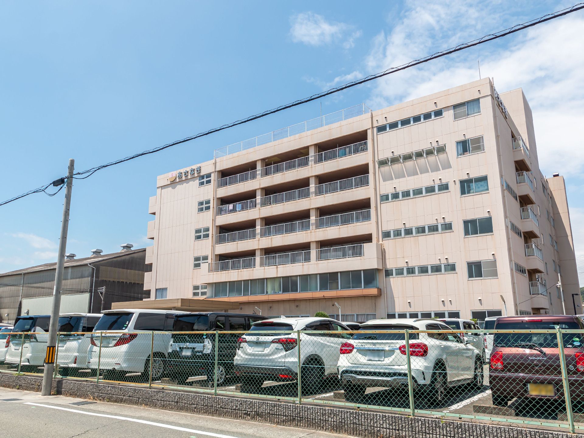 車がたくさん止まった駐車場に隣接しているベージュの外観の建物