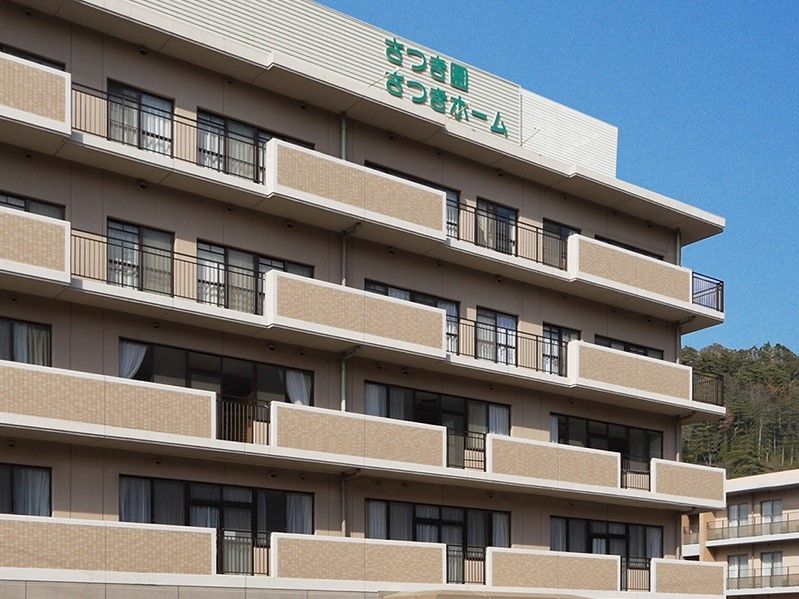 ベージュの大きな建物の外壁にはグリーンでハウス名が書かれ、周辺には自然も多い。
