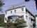 白い外壁の3階建ての建物には三角屋根が付き、周りにはたくさんの緑が植えられている。