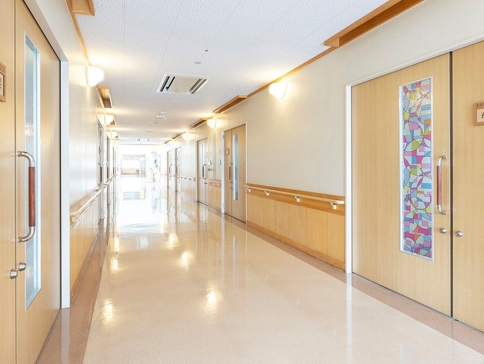 両サイドに手すりが設置された幅の広い廊下。居室のドアはスライド式で、ステンドグラス風の窓が付いている。
