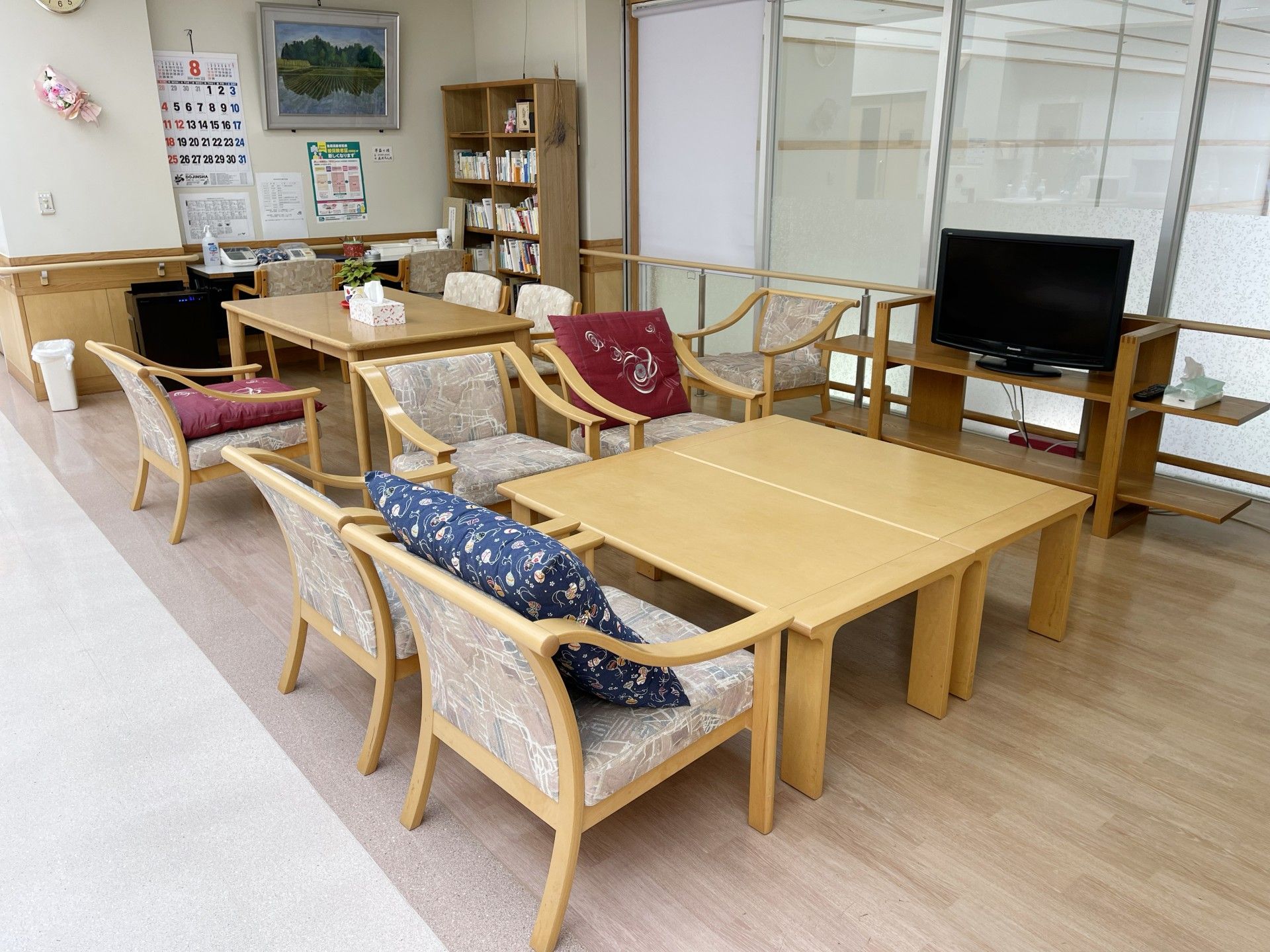 カルテのようなものを見ながら高齢女性に説明をしているピンクのエプロンを付けた若い女性スタッフ。