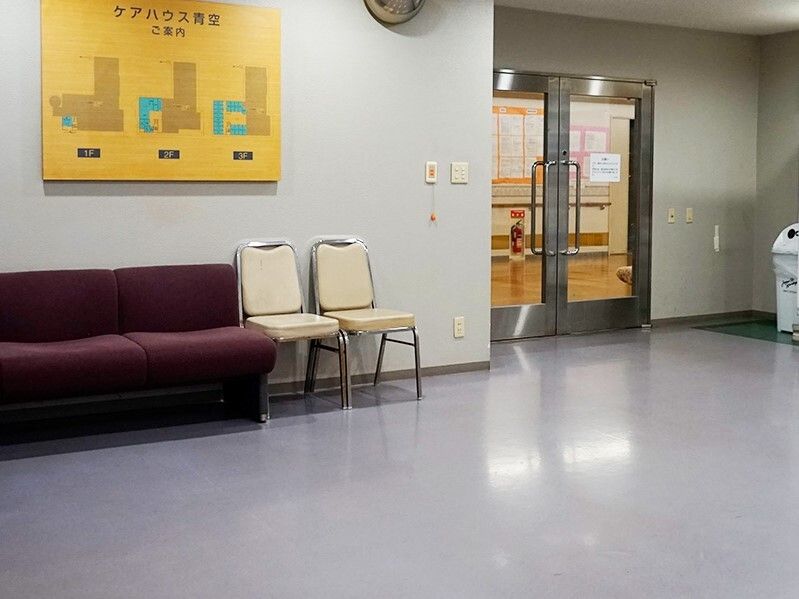 エンジのソファやベージュの椅子が置かれ、壁には館内の案内図があり、右奥にはドアがある。