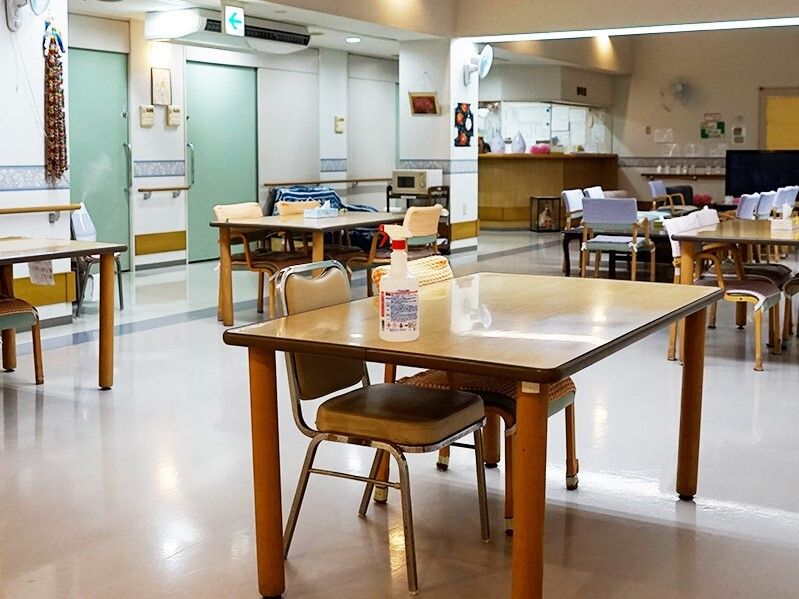 木製のダイニングテーブルが複数置かれた食堂は明るい雰囲気。テーブルの片側にだけ椅子が設置されている。