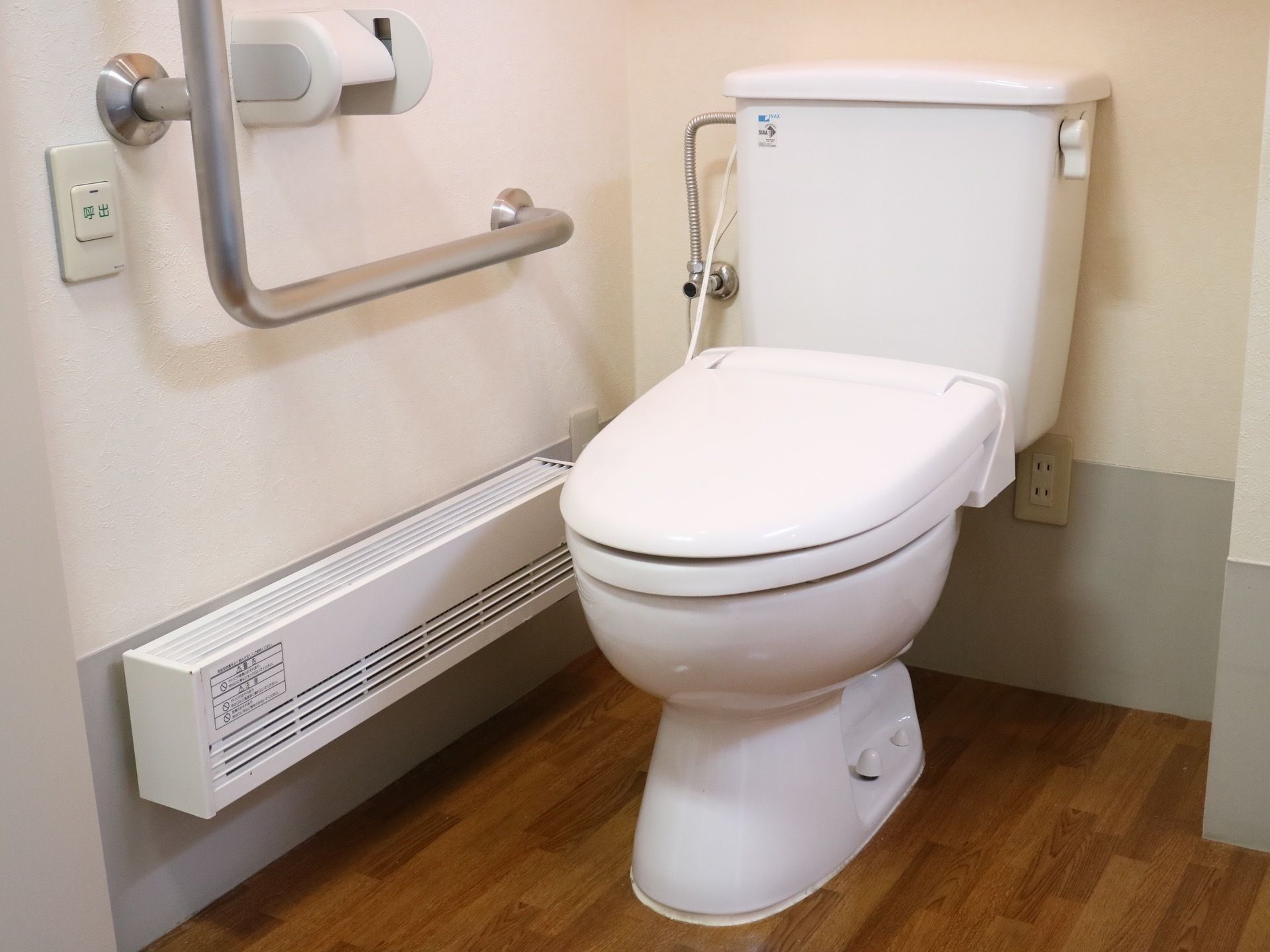 白色と木目調の落ち着いた雰囲気のトイレである。手すりが備え付けられているので、転倒リスクが抑えられ、安全に使用できる。