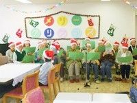 高齢者がサンタ帽をかぶって歌を歌っている様子。クリスマス会の一場面