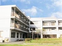 鉄骨造３階建ての建物の外観写真。緑が植えてある中庭の様子も見えている