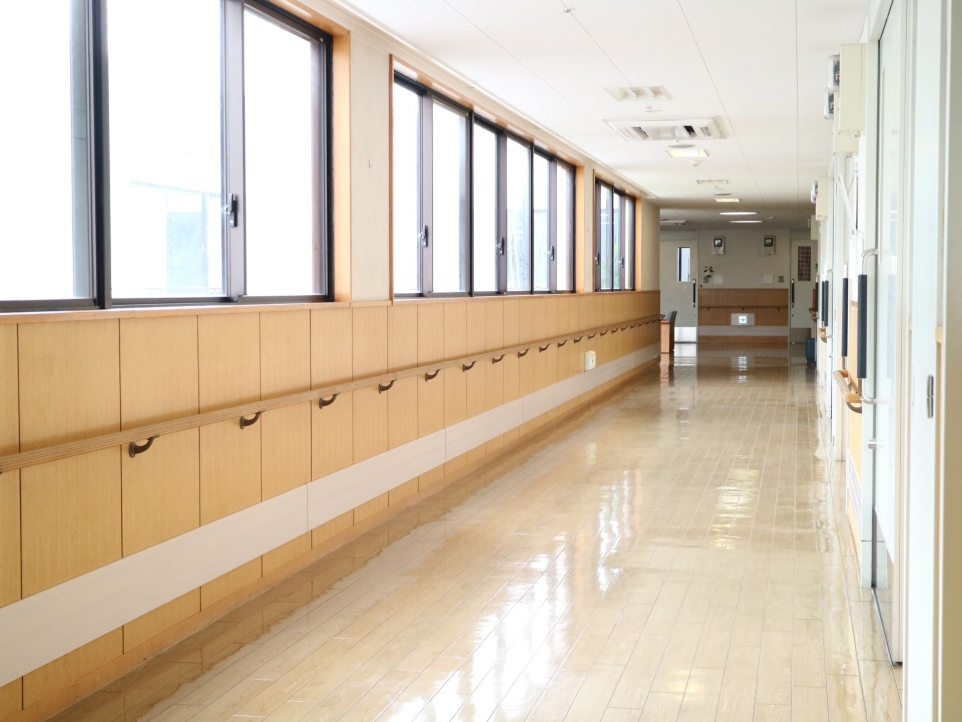 廊下がまっすぐ伸びている。居室ドアが無い窓側の壁に取り付けられている手すりは、切れ目なく続いている。