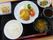 黒いお盆に食事が乗っている。メインは揚げ物で、レタスとトマト、レモンが添えられている。小鉢の副菜、ご飯、汁物がある。