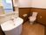 フローリングと壁半分がダークブラウンになっている広いトイレがある。側には鏡と収納棚がついている洗面台が置かれている。