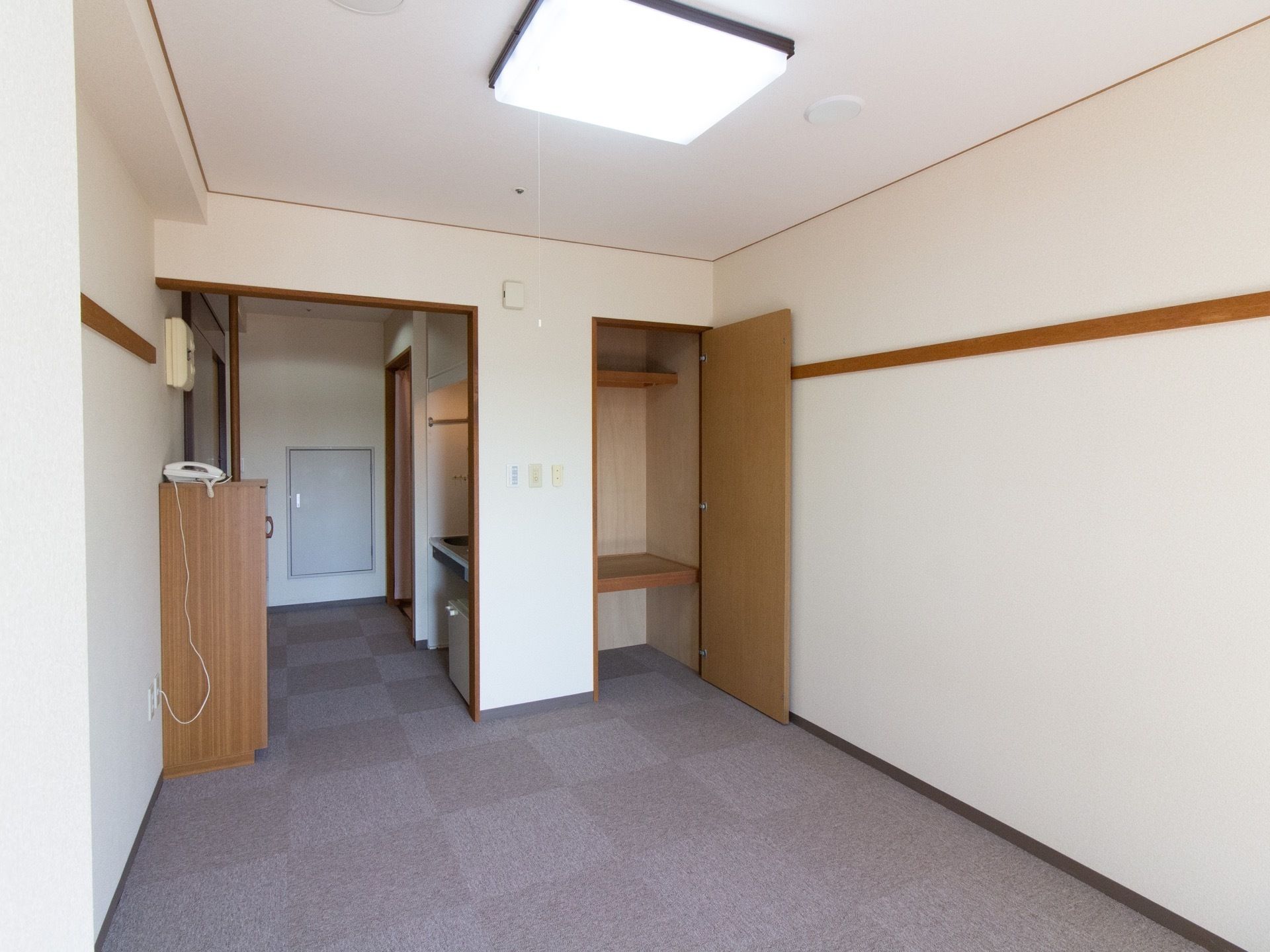 カーペット敷きで、白い壁に囲まれた居室である。キッチンや収納が備えつけられ、照明や電話が設置されている。