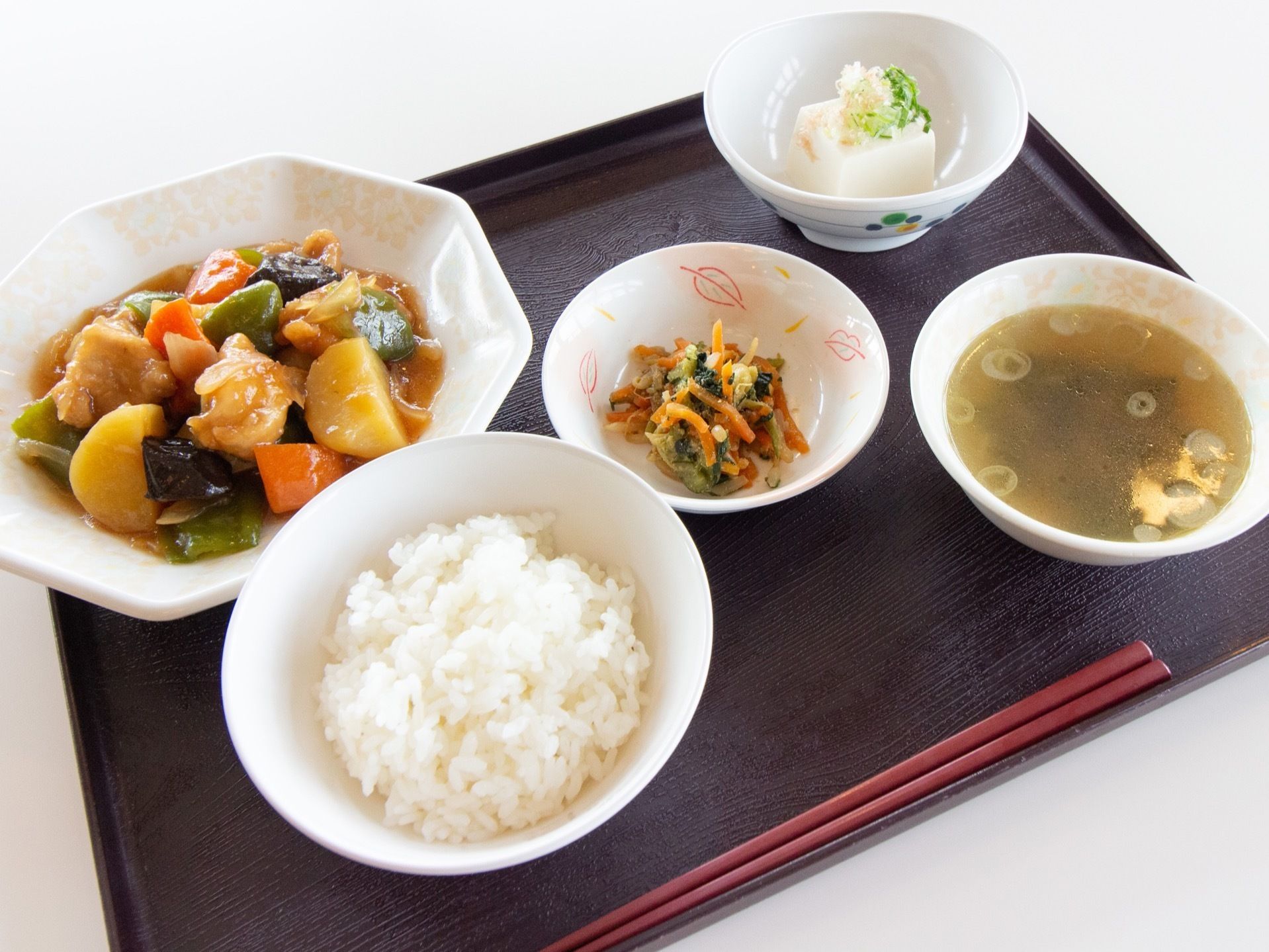 施設の食事である。ご飯、汁物、主菜、副菜の５品と、お箸が１膳、お盆に乗せてある。野菜や肉類バランスよく作られている。