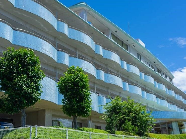 ベランダ付きの大きな建物は白とブルーでまとめられ、建物の周辺には緑が多く植えられている。