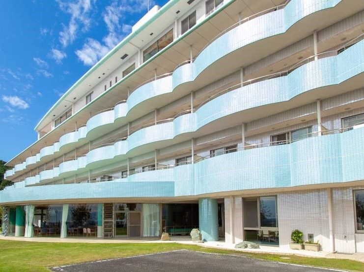 敷地内には広い庭と駐車場があり、各フロアにベランダがあり、空には青空が広がっている。