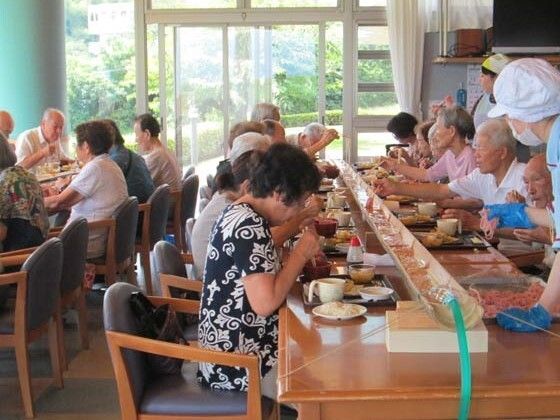そうめん流しがセットされた食卓を囲み、そうめんを食べている入居者たち。大きなテーブルの中央に長い竹が置かれている。