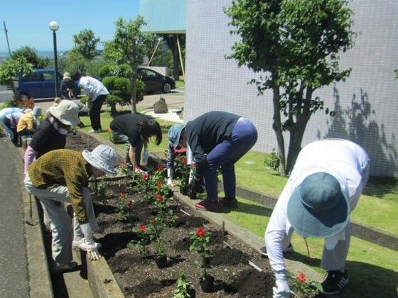 高めの花壇に赤い花の苗を植えている入居者たち。みな長袖に帽子をかぶり、手袋をはめている。