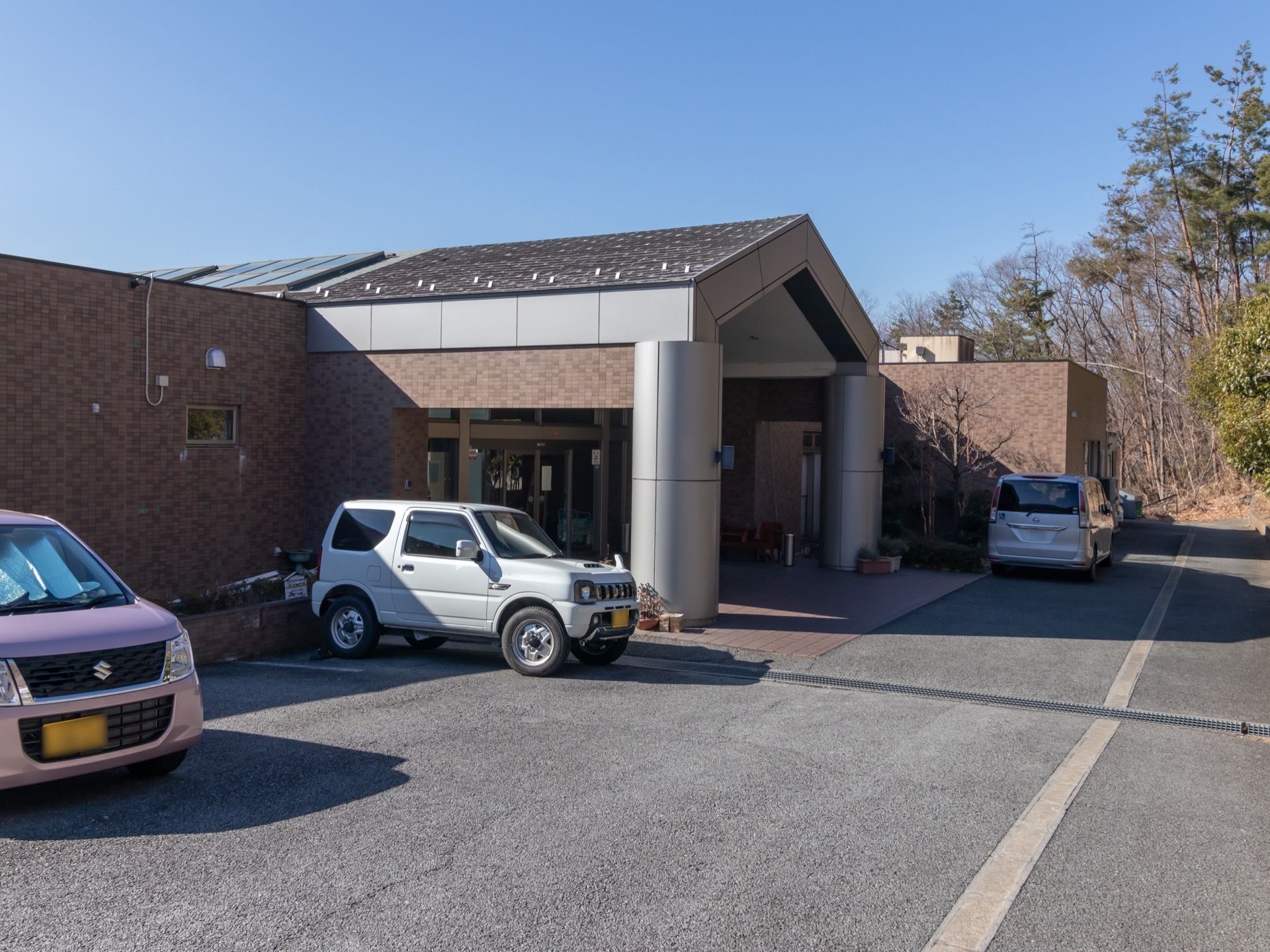 緑の中に建てられている施設建物。平屋建てだが土地に余裕があるため、敷地内には広い駐車場が設けられている。