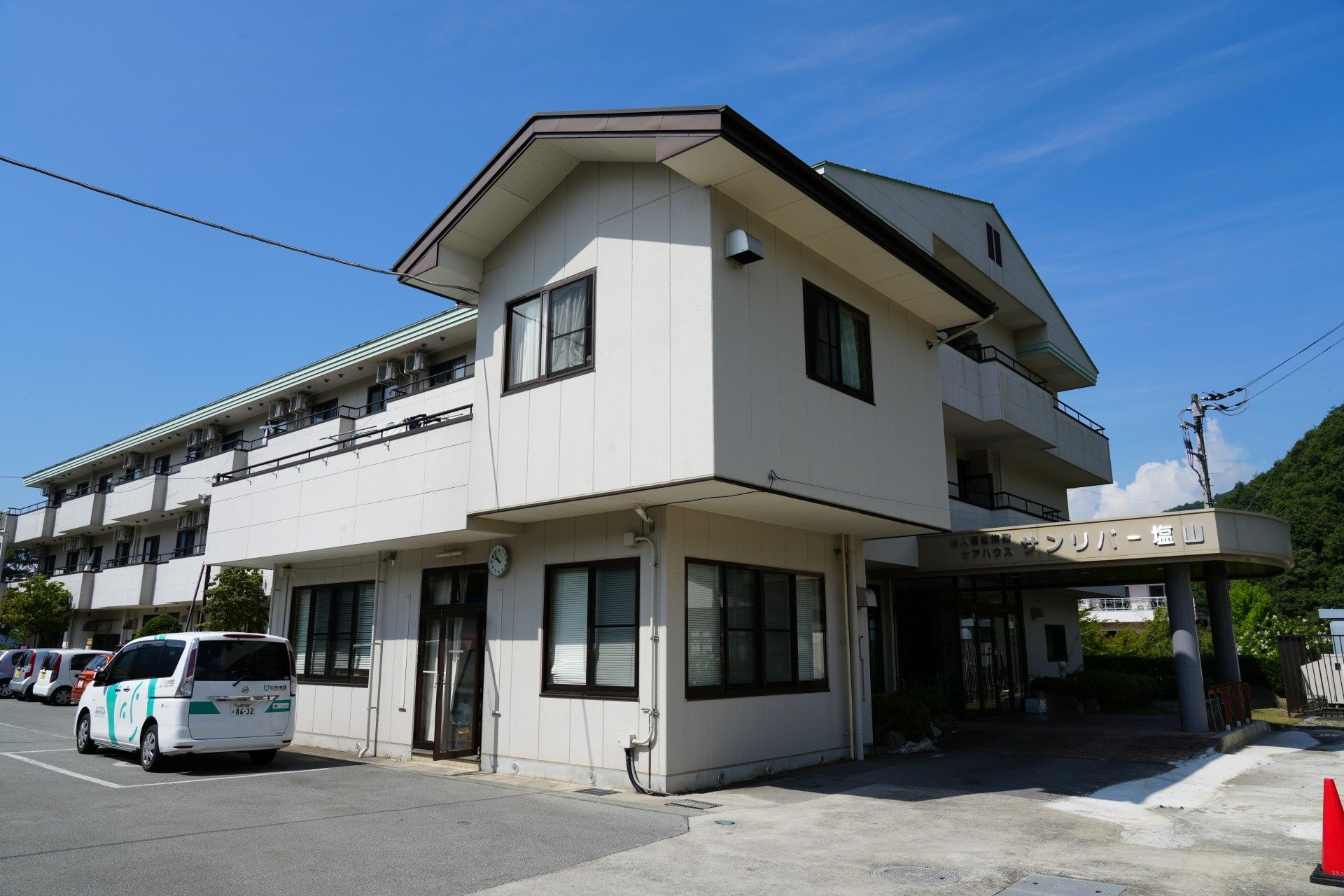 ３階建ての白い外観の建物が建っている。敷地内はバリアフリーになっていて、道路もきれいに舗装されている。