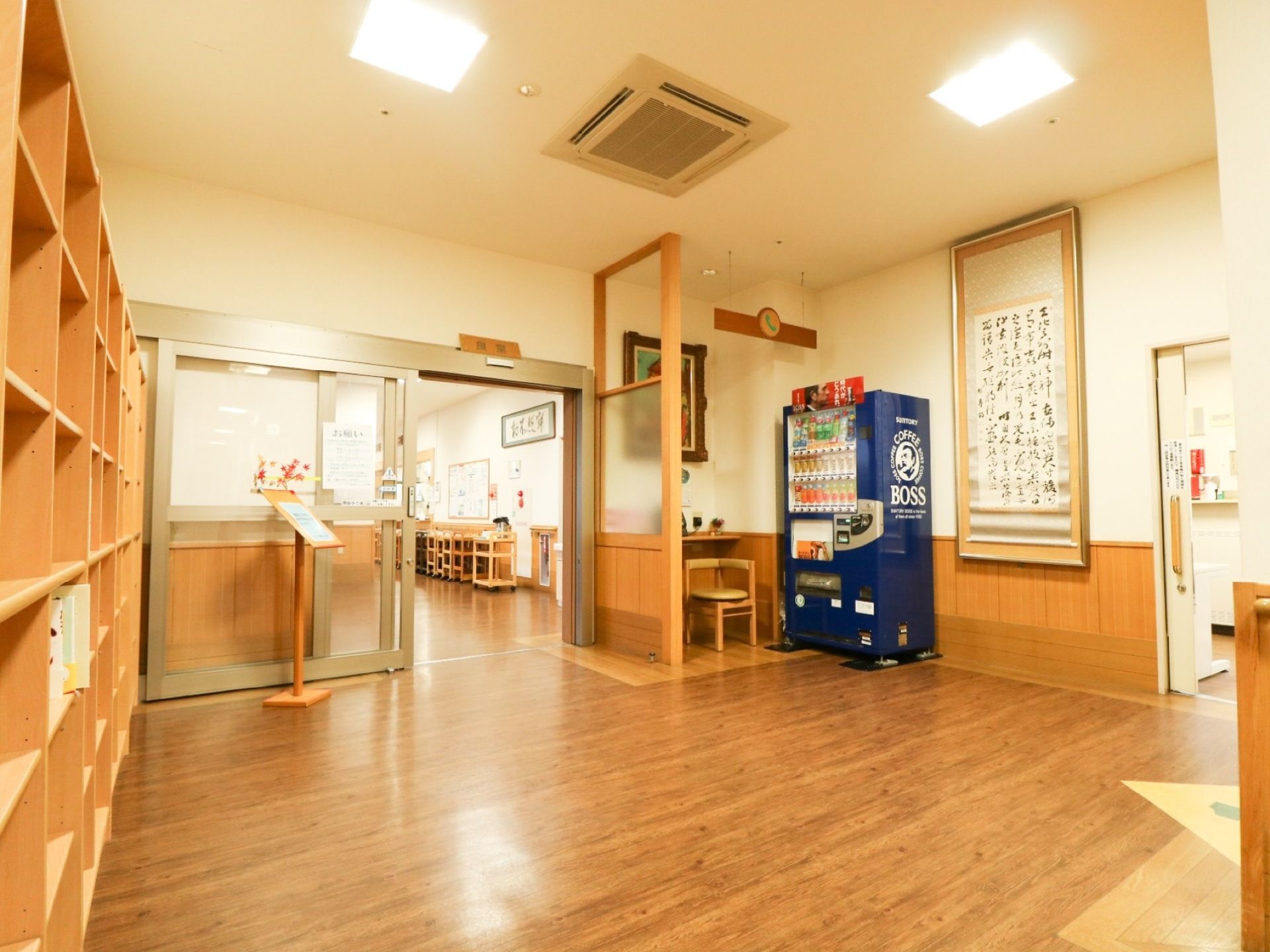 施設内に飲料の自動販売機がある。その横の壁に、縦長の書道作品が飾られている。食堂の入口は自動扉になっている。