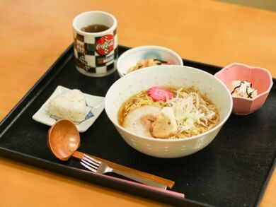 黒色のお盆に、ラーメン、おにぎりの他に、おかずの小鉢が２つとお茶が載っている。手間には、箸、スプーンとれんげが置かれている。