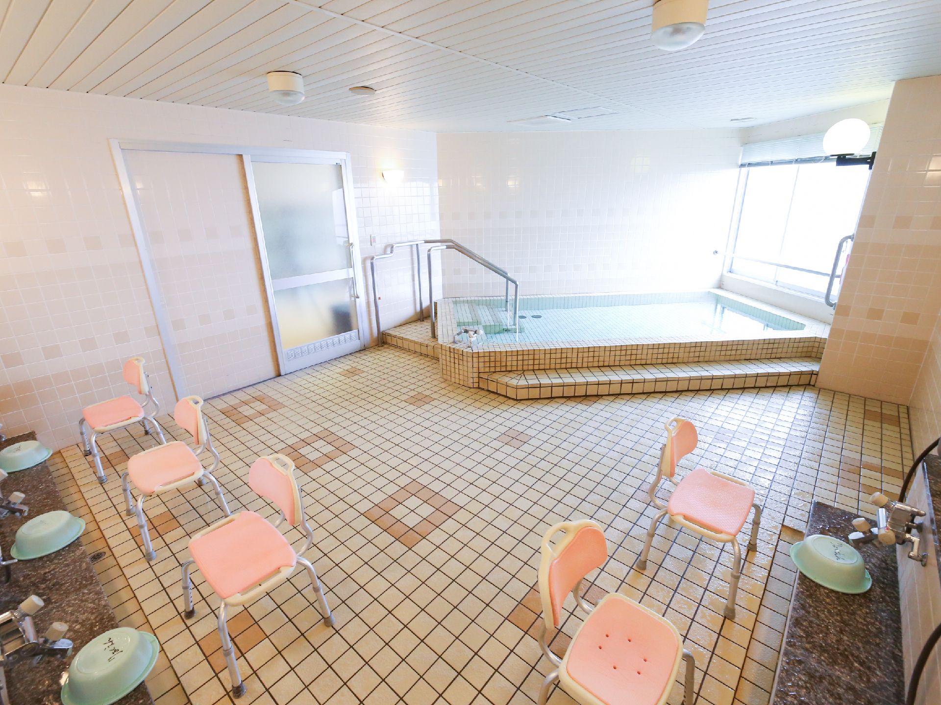 シャワーチェアが並んでいる大浴場の設備写真。鏡の両横に立ち上がり用の手すりがある