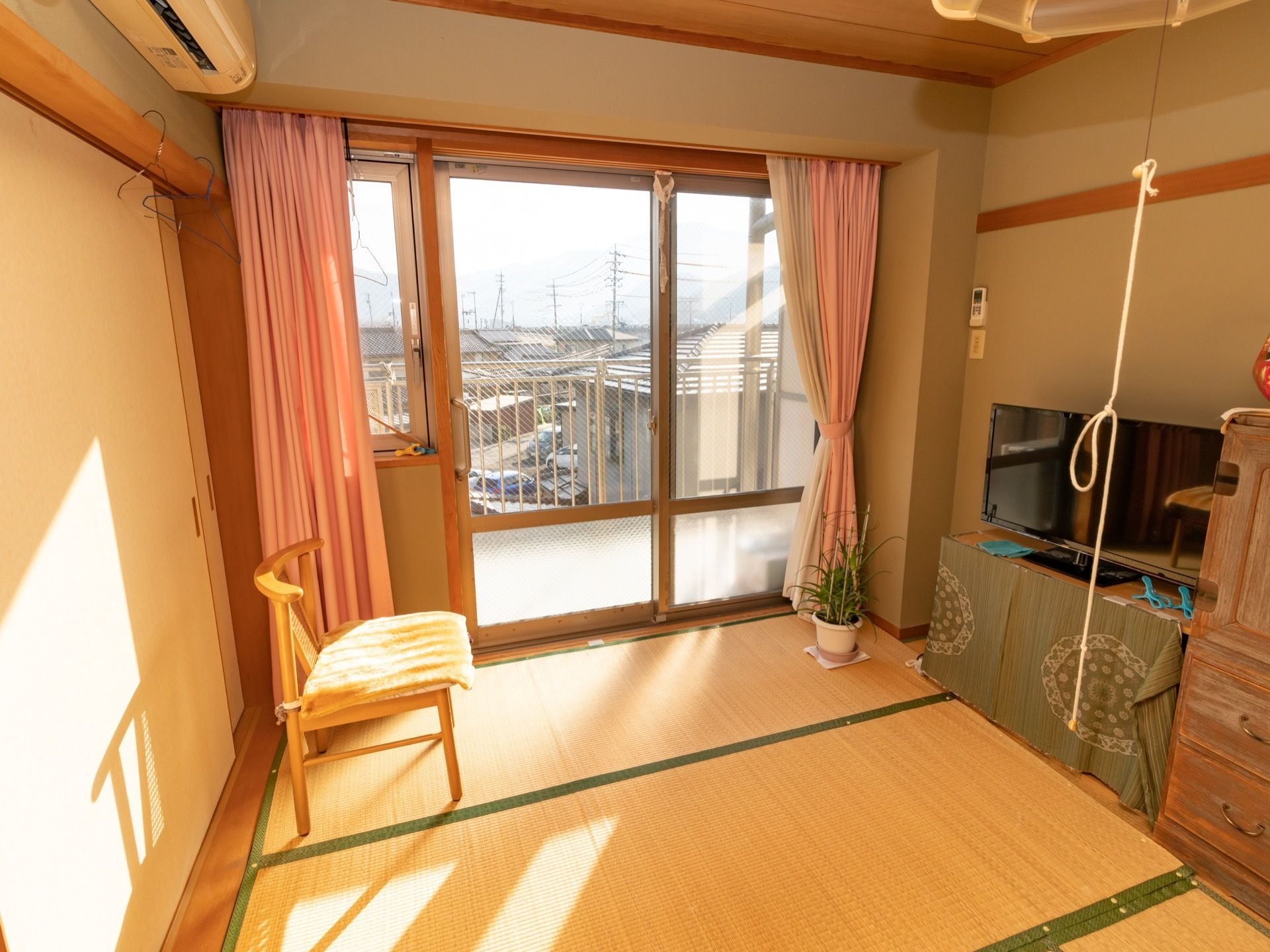 畳の敷かれた部屋に、テレビとタンスが置かれている。椅子が１つ置かれていて、壁にはエアコンが設置されている。