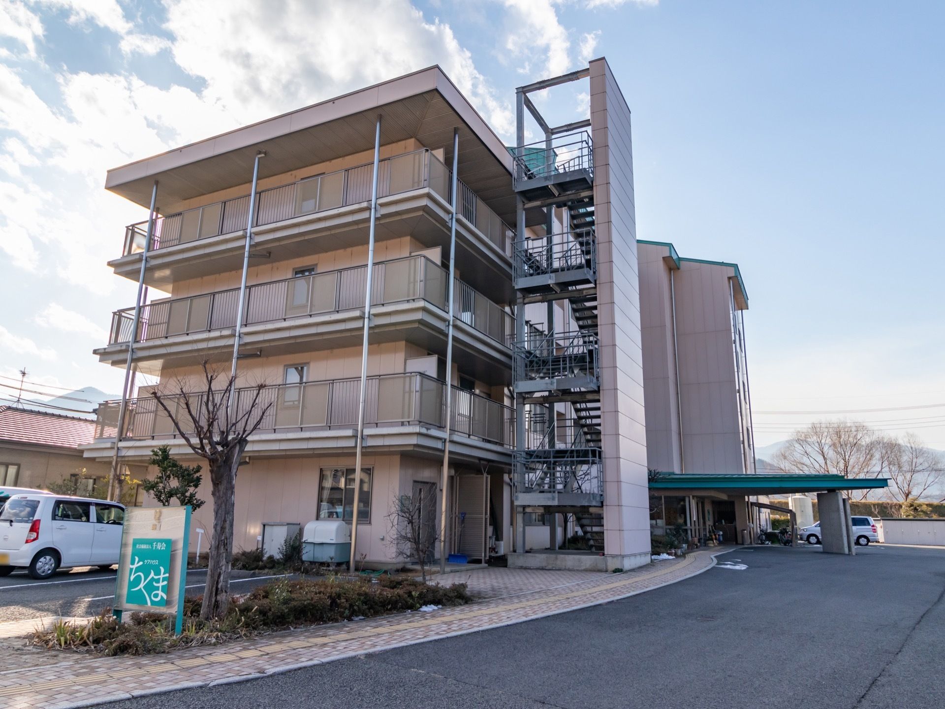 広い駐車スペースや車寄せができるアプローチが付いた５階建ての建物がある。非常用の外階段が設置されている。
