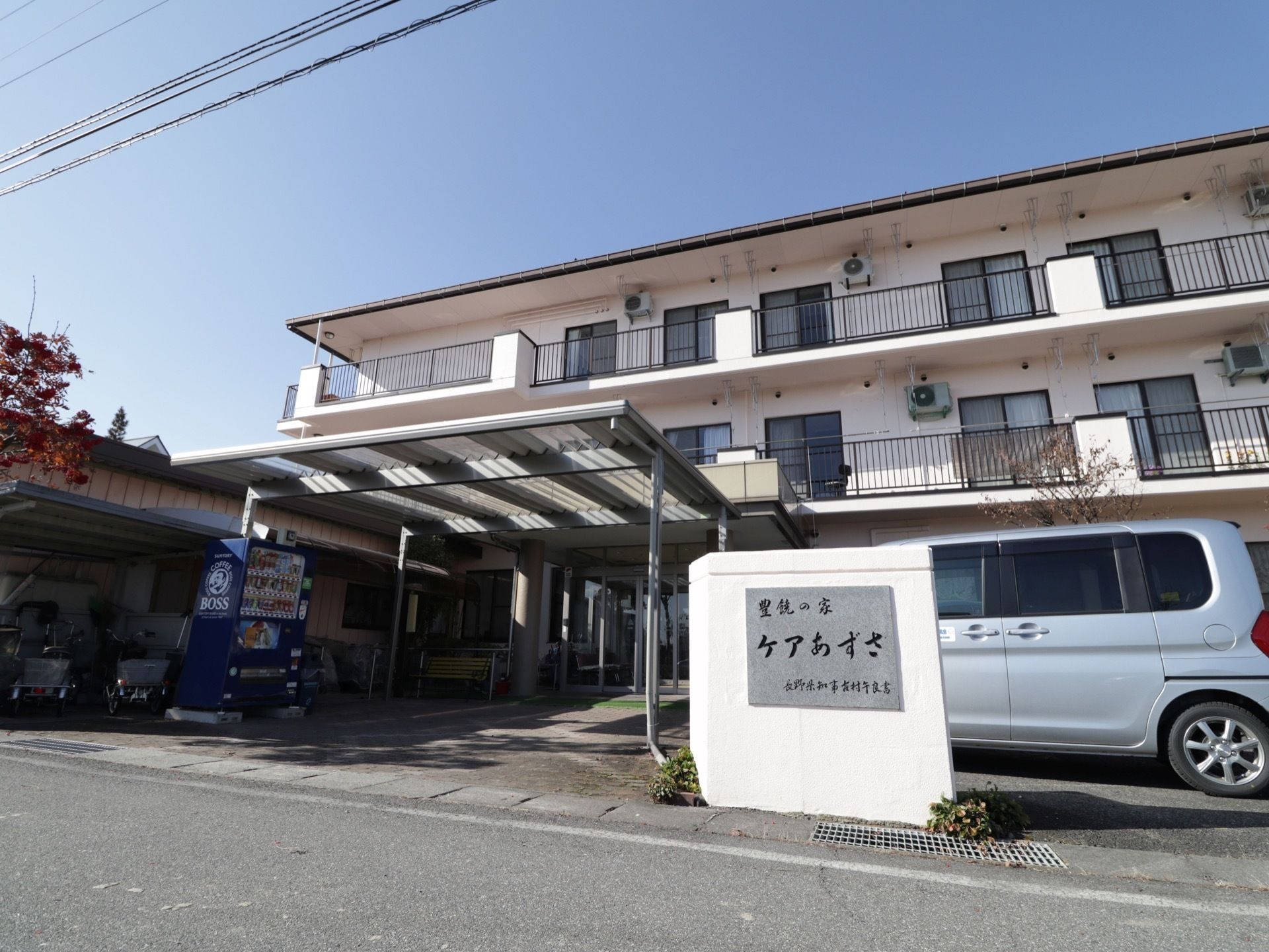 施設は白い外壁で、３階建ての建物になっている。玄関までの通路の脇には、自動販売機が１台設置されている。