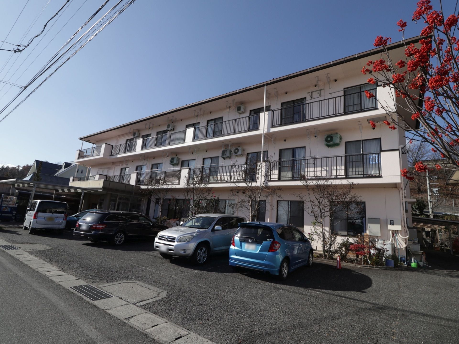 施設は白い外壁の３階建ての建物である。各居室にはベランダが設置されている。建物の前には駐車スペースが確保されている。