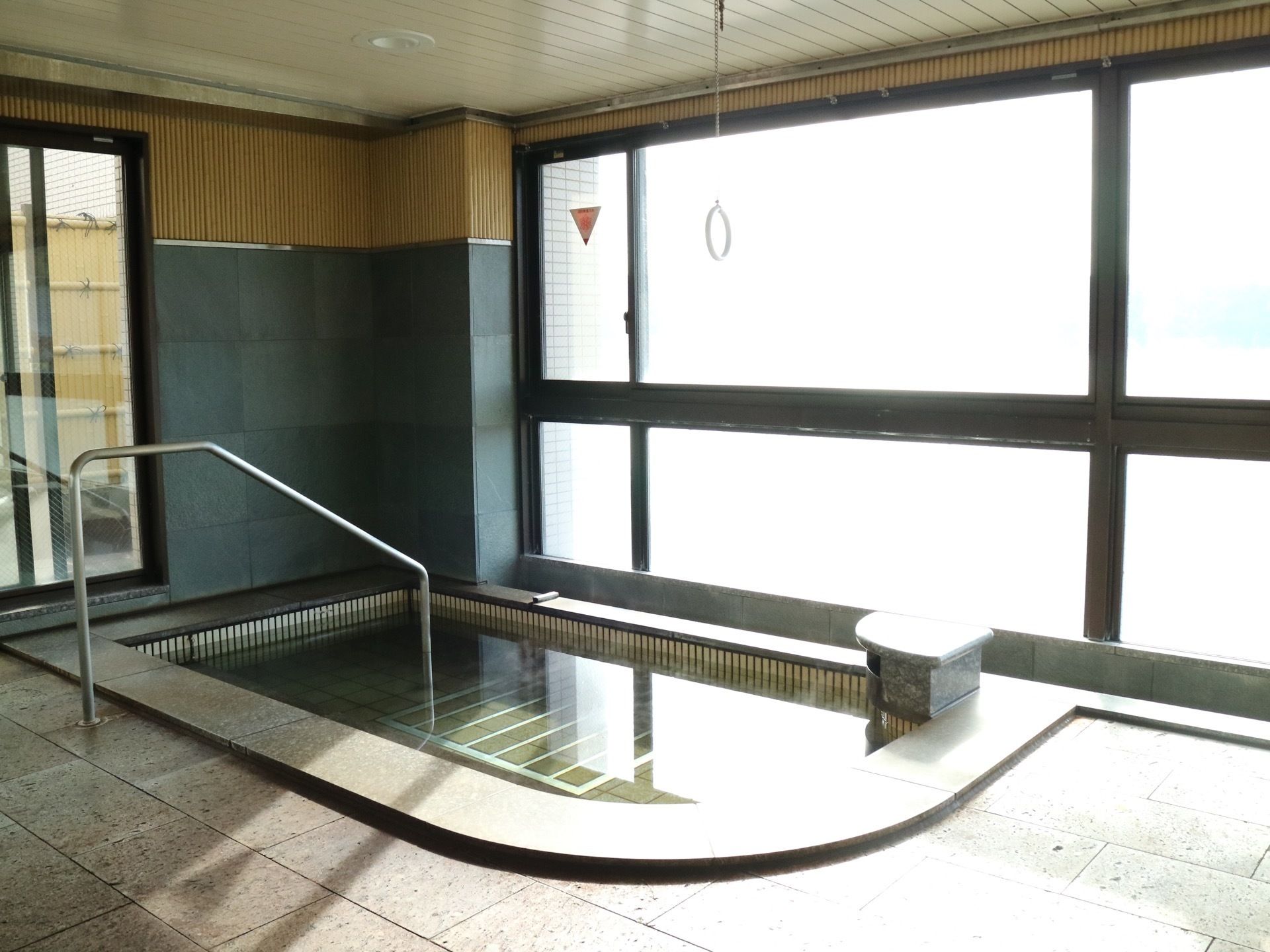 窓が大きく設置されている浴室である。石材造りの浴槽が完備され、手すりを持って浴槽へ入ることが出来る。