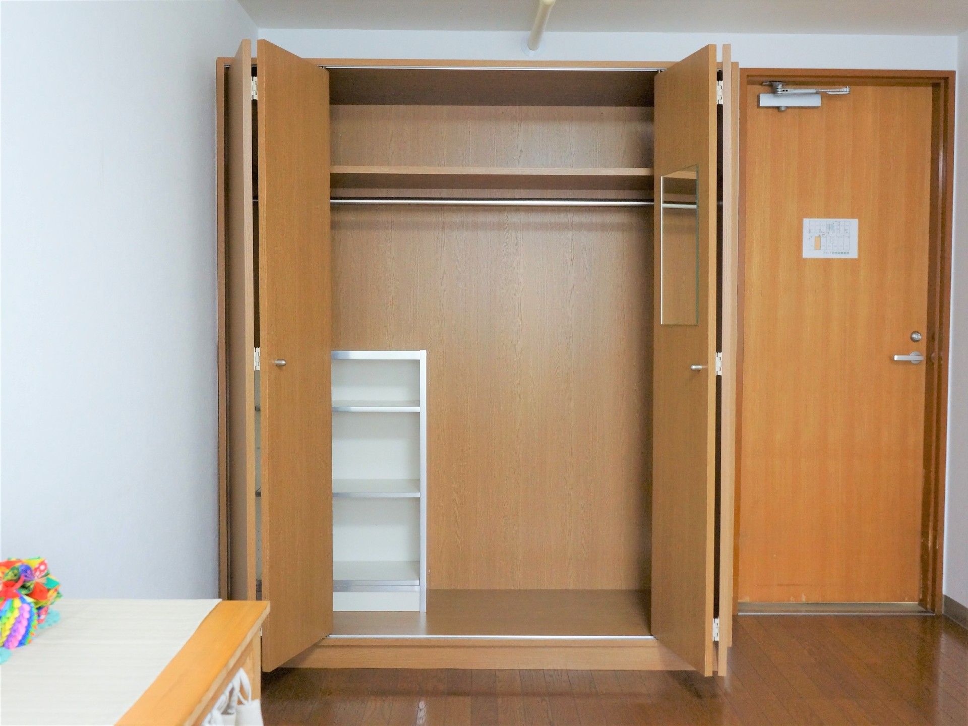 部屋には両開きの扉がついている大きなクローゼットがある。中は2段あり、下の段には白のカラーボックスとハンガーをかけるポールがついている。