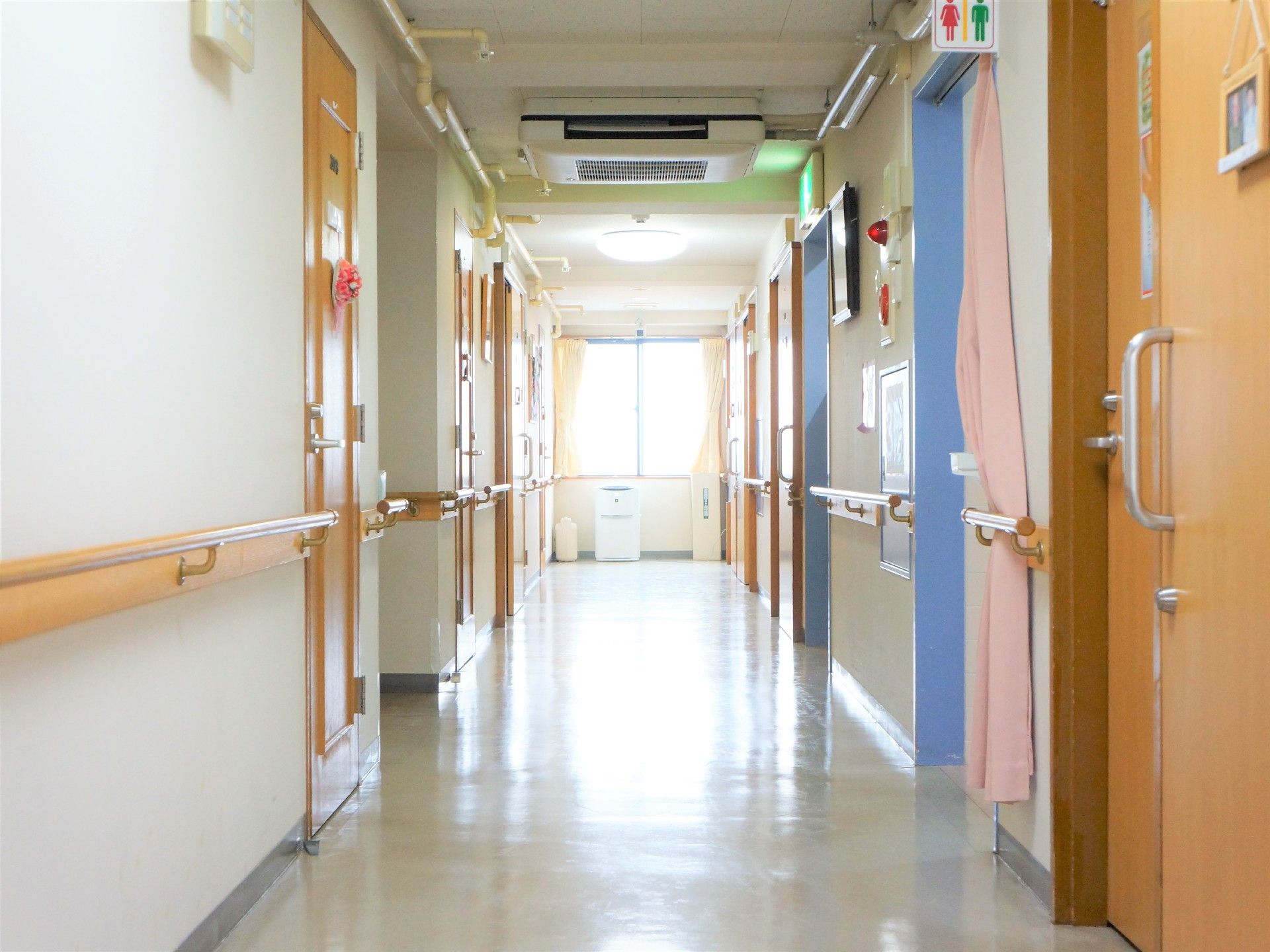広々とした廊下の両側の壁には、手すりがずっと伸びている。個室やトイレのドアがあり、各ドアにはそれぞれ違った飾りが掛けられている。