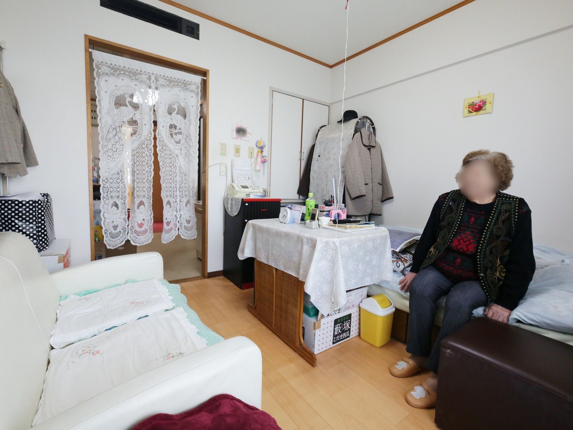 入居者様のお好みにレイアウトされた居室である。白いソファーが置かれ、ベッドの上に腰掛けられている女性の入居者様の姿が見える。