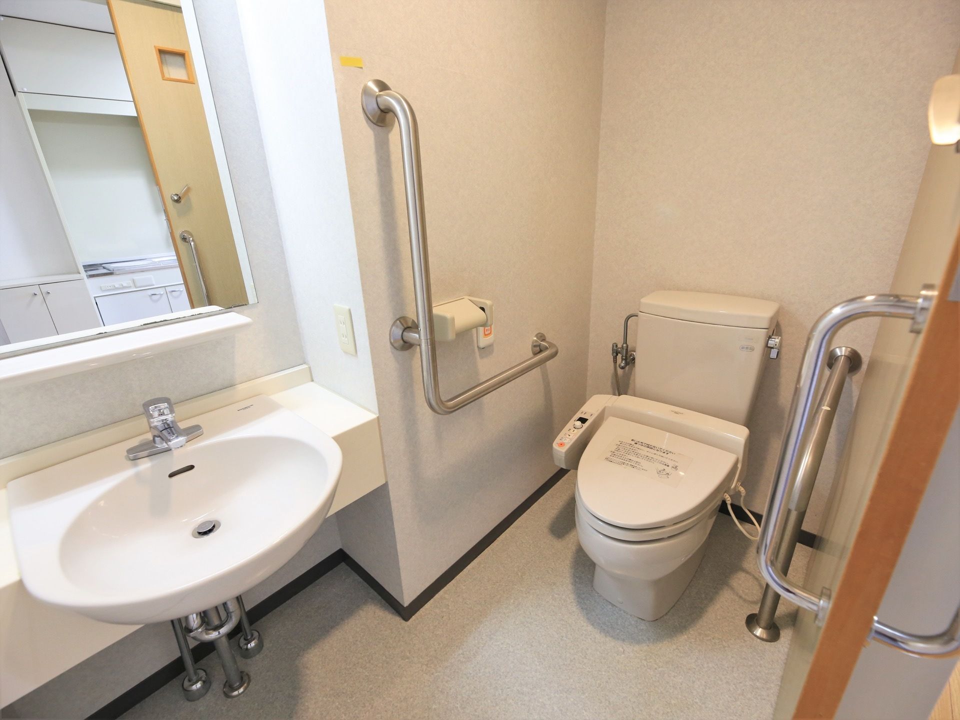 右手前に引き戸の入口がある。温水洗浄便座を設置したトイレが中央にあり、壁には手すりと非常ボタンがある。