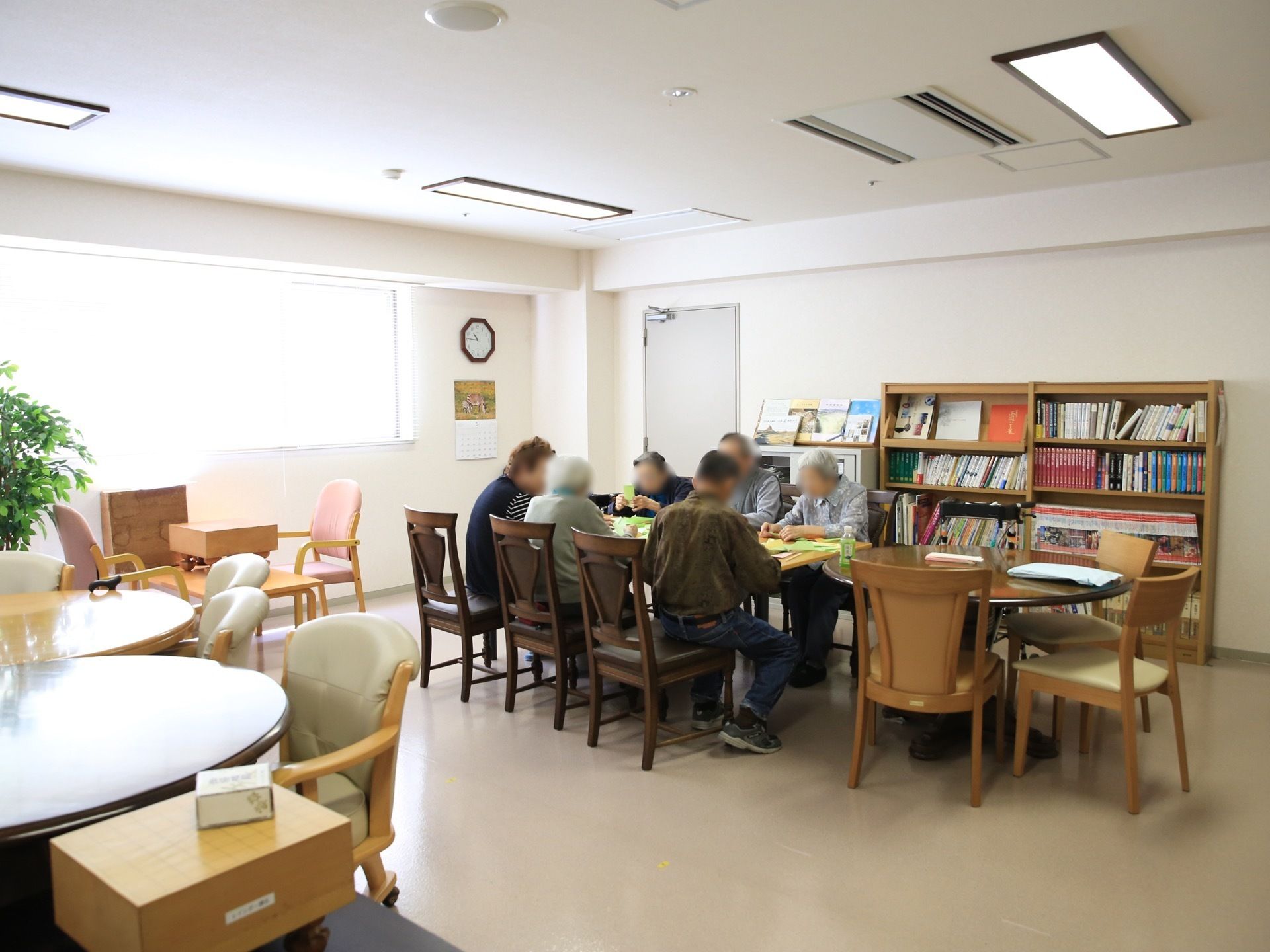 丸いものや四角いもの、さまざまな形のテーブルが並べられた共有スペースで、たくさんの入居者様が作業をしている。