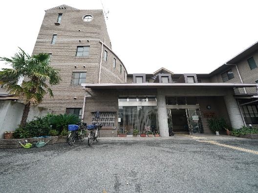 玄関の横には花壇があり、自転車が２台止められている。自動ドアが設置され、屋根も付いている。