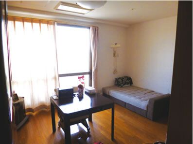 緊急通報装置が付いた部屋には寝具付きのベッドやテーブルセットが置かれ、窓にはカーテンが付いている。