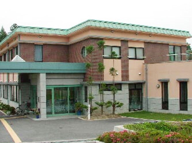 駐車場や庭スペースが付いた2階建ての建物。茶色と緑の外観で、ナチュラルな雰囲気。