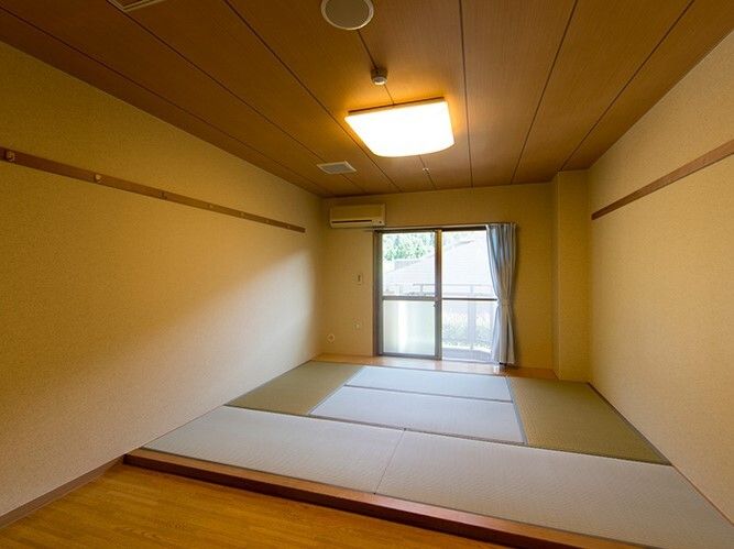 畳敷きの和風の部屋にはエアコンや和風の照明が付き、手前には床間もある。窓にはカーテンも付いている。
