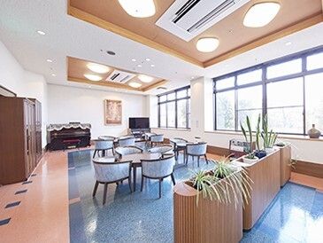 カーテンのない大きな窓が付いた共有スペースには、ブルーの応接セットが複数あり、奥にはピアノも置かれている。