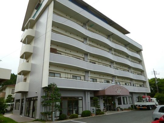 シルバーの大きな建物の各フロアにベランダがあり、玄関の屋根の部分にはハウス名が書かれている。