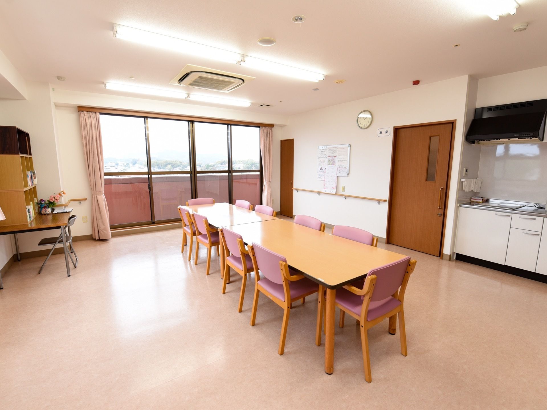 広さが十分にある白を基調とした食堂である。５人掛けのダイニングテーブルが２台並べてある。同じスペースにシステムキッチンが完備されている。