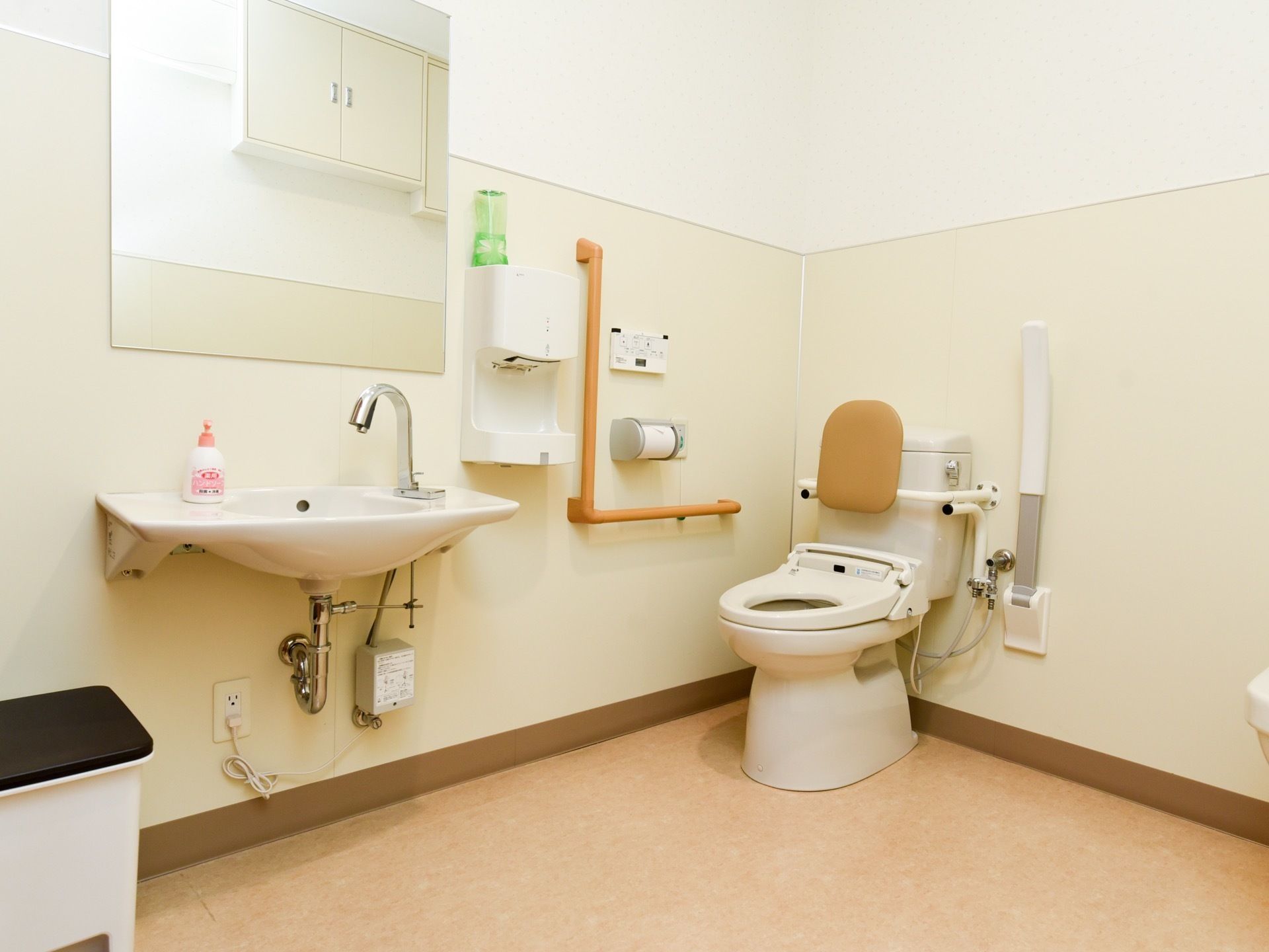 広々とした清潔感のある共用トイレである。温水洗浄便座や洗面台、ドライヤー、手すり、ゴミ箱が完備されている。