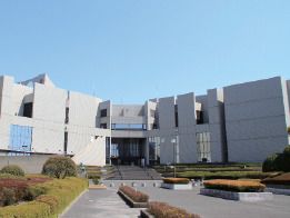 白を基調とした大きな建物は横に長く、手前にはたくさんの草木が植えられ、駐車場もある。