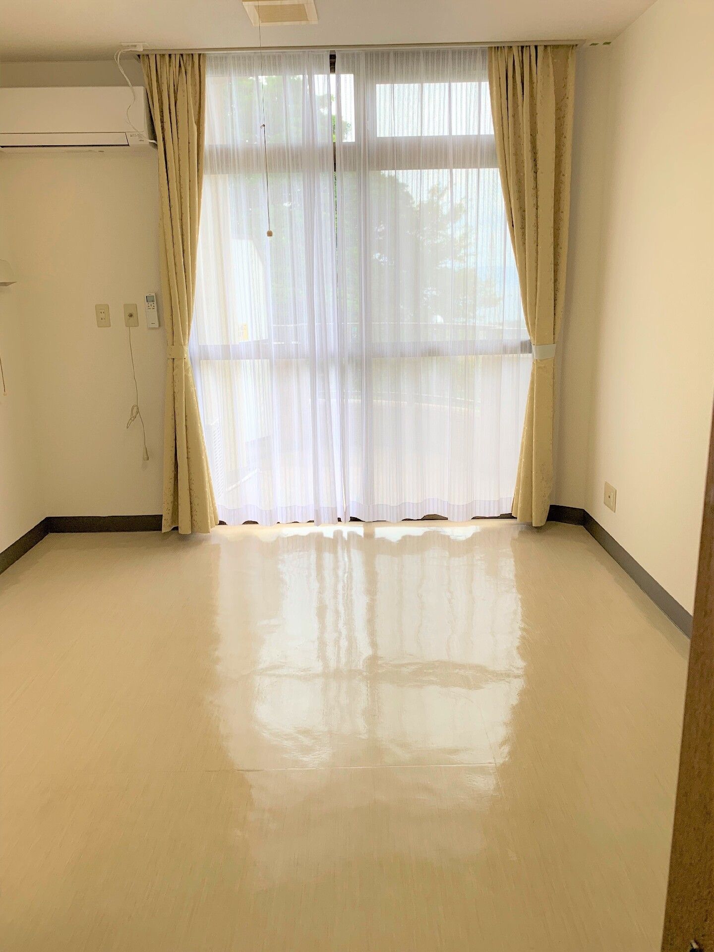 壁には緊急通報装置があり、エアコンも完備。家具や家電はなく、大きな窓にレースカーテンとカーテンが付いている。